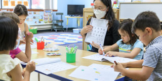 An early childhood educator shows a math workbook to a table of young learners.