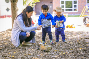A teacher plays with two young children in an outdoor playground.